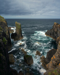 Rocky cliffs and ocean waves on the Isle of Harris and Lewis, Scotland. Dramatic coastal landscape with rugged rocks, turquoise water, and overcast sky.
