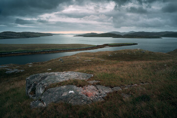 Dramatic coastal landscape of the Isle of Harris and Lewis in Scotland. Overcast sky, rocky terrain, and calm sea in the Outer Hebrides islands.