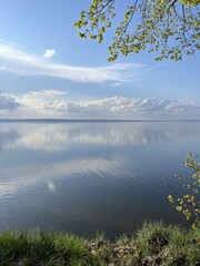 Wide expanses of the Volga River: the sky is reflected in the quiet surface of the water, view from the green forest. Volga region, Ulyanovsk, Russia.