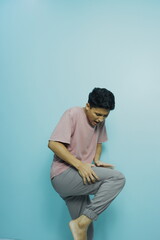 Young man grimacing and holding his knee in pain against blue background