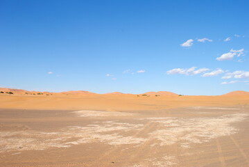 A desert landscape with a blue sky and footprints in the sand