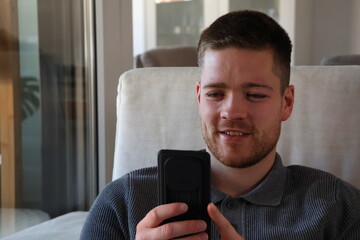 adult man sitting on couch laughing while looking at smartphone at home