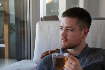 man drinking tea on couch while looking out of window at home