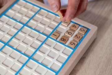 closeup hands carefully placing number into Sudoku puzzle, senior man focused on solving puzzle on...