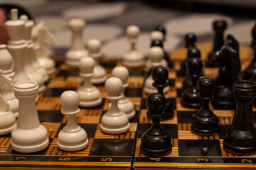 Detailed view of wooden chess set with white and black pieces positioned on checkered board showing mid-game position with shallow depth of field. Concept of strategic board game and mental challenge.