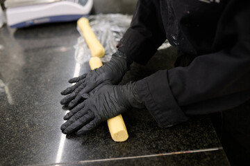 Chef in black gloves skillfully rolling dough on a polished countertop, showcasing culinary techniques and attention to detail in a professional kitchen
