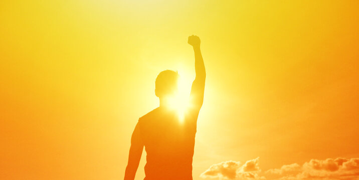 Silhouette of a man raising his fist in the air against a bright sunrise, symbolizing success, victory, confidence, and motivation.
