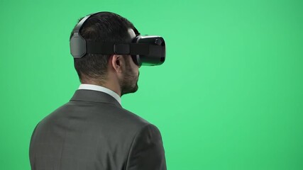 Rear view of an African American businessman wearing a virtual reality headset standing against a vibrant green screen exploring immersive digital experiences and future technology. - Powered by Adobe