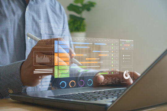 Businessman using digital tablet and laptop analyzing Gantt chart and project data dashboard. Concept for project management, productivity tracking and workflow planning in modern business.