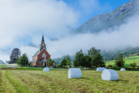 Picturesque Norwegian church in morning fog among green mountains and fields