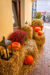 A cozy autumn decorative composition with pumpkins, hay bales, chrysanthemums, and lanterns. A seasonal installation decorating an entrance for Halloween or Thanksgiving.