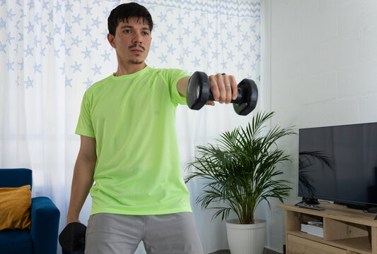 Man performing a front raise exercise with one dumbbell, arm extended forward. Concept of strength, home workout, and healthy lifestyle