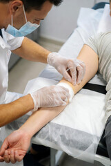 Obraz premium Professional healthcare worker in face mask and gloves carefully applies a bandage to a patient's arm after a medical procedure in a clean clinic setting.