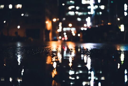Abstract reflections of colorful city lights shimmering on wet urban street pavement at night, creating a moody bokeh background.