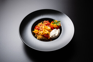 Plate of linguine pasta with cherry tomatoes and buffalo mozzarella on a black background