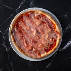 top view pizza with speck slices on black marble background