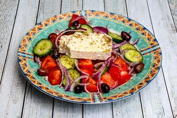 A Greek salad with a large piece of feta cheese and tomatoes, onions, olives and cucumber in a pretty dish