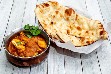 Aloo Gobi, cauliflower and potatoes in a traditional Indian copper dish of with a piece of batura naan bread
