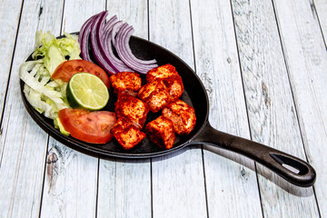 Indian food Tikka chicken in a cast iron skillet served hot at the table garnished with onion, cucumber and tomato