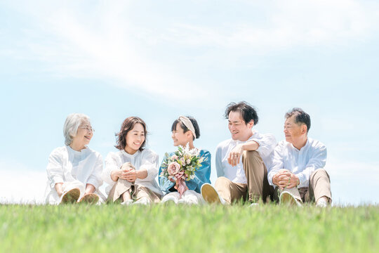 A park with a view of the blue sky, a family sitting on a hill, parents and children, a three-generation family (father, mother, daughter, grandmother, grandfather)
