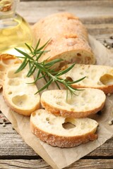 Ciabatta slices, oil, peppercorns and rosemary on wooden table, closeup