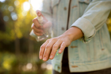 Woman spraying tick repellent onto hand in park, closeup
