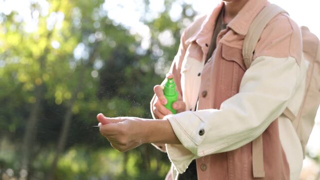 Woman spraying tick repellent onto hand in park, closeup