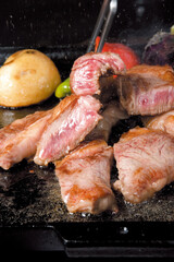 牛肉を鉄板焼で焼いているイメージ写真｜Sizzling Beef Grilled on a Teppan Hot Plate Against a Black Background