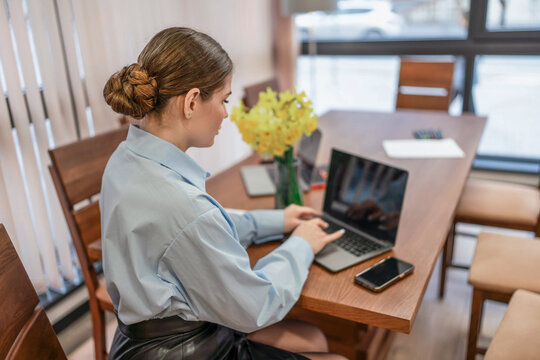 Woman typing laptop, professional works remotely at wooden office table with flowers. - Powered by Adobe