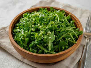 Wooden bowl filled with green salad of lettuce, peas and herbs on linen cloth over marble surface, side view in soft natural light for menu use.