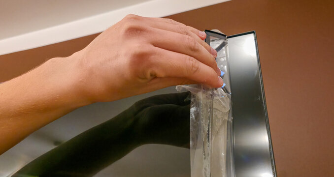 A man is peeling off the protective film from a screen in close-up. Protective film for expensive items and electronics.