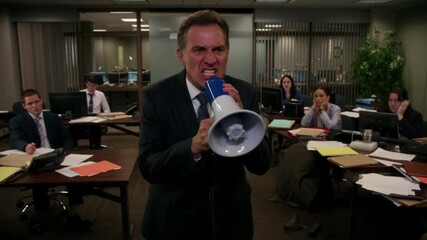 A businessman is speaking into a megaphone in a corporate office, with several colleagues looking in concern. The man appears to be angry while yelling through the megaphone Stock Video - Powered by Adobe