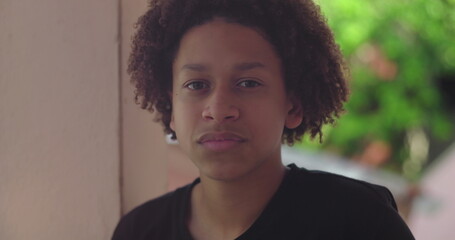 Young Hispanic boy of African descent with curly hair, looking directly at camera, close-up...