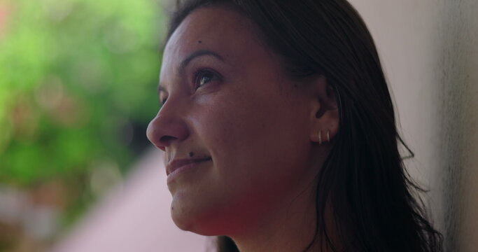 Serene woman gazing upward with subtle smile, wearing hoop earrings, close-up against blurred green background, introspective and calm moment captured in profile