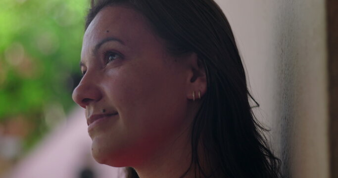 Serene woman gazing upward with subtle smile, wearing hoop earrings, close-up against blurred green background, introspective and calm moment captured in profile