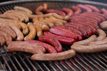 Photo of process of cooking chicken sausages and beef meat on grill on metal grate over coals at fast food cafe, city holiday Tbilisoba, New Year fair, street market, harvest autumn festival. Lunch