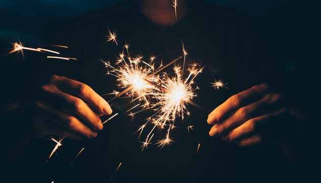 Hands holding bright sparklers creating magical light trails and festive sparks for celebrations and joyous moments