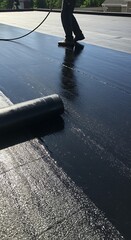 Worker applying new roofing material on a flat roof, ensuring waterproof protection for the building.