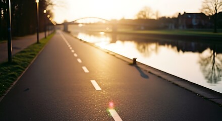 Pathway beside river at sunset with bridge and trees.