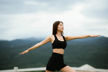 Fototapeta premium A woman standing outdoors with eyes closed, breathing deeply and stretching her arms, embracing calmness and nature.