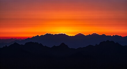 Fototapeta premium Silhouette of mountains against a vibrant orange and red sunset sky, creating a dramatic landscape.