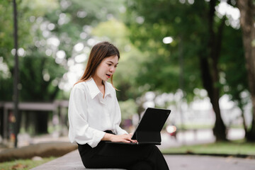 Business woman sitting outdoors smiling while using smartphone, working or chatting in modern city environment with blurred background lights.