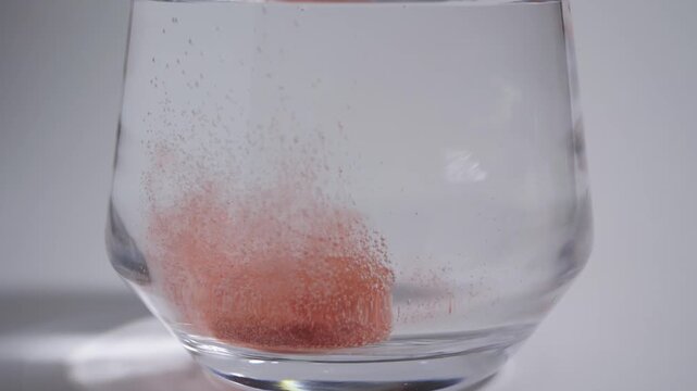 A red effervescent tablet dissolving in a glass of water, creating a cloud of tiny bubbles.