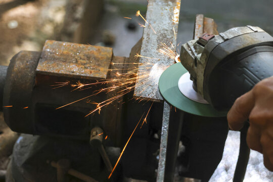 Focused worker grinding metal with power tool in workshop. Bright hot sparks fly from steel as machine works, showing powerful and dangerous industrial process