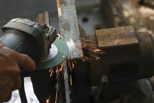 Focused worker hand uses an angle grinder for cutting metal clamped in vise. powerful tool creates shower of bright sparks from steel in workshop