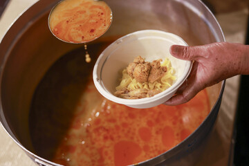 Volunteer hand serving hot soup from large pot with ladle. food donation showing charity and help...