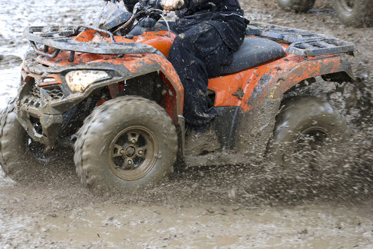 Exciting outdoor adventure with person riding an all terrain vehicle on muddy trail. orange quad bike splashes lot of dirt, thrilling and dirty motorsport activity