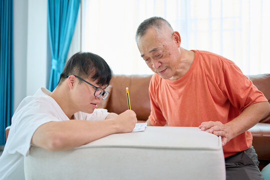 A man with Down syndrome is sitting at home doing his math homework with his teacher