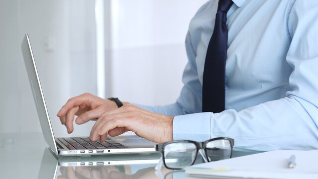 Businessman working on laptop in modern office, typing on keyboard and concentrating on corporate projects. Business and technology conceptal corporate tasks. Business people concept - Powered by Adobe