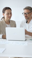 Obraz premium Businessman and adult businesswoman reviewing marketing analytics on laptops, working together strategically in contemporary workplace with minimalist interior design and collaborative atmosphere